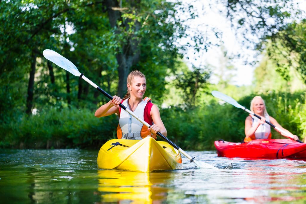 two friends kayaking in a river surrounded by forest.
